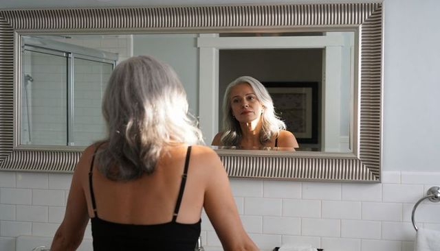 Mature woman reflecting in silver-framed bathroom mirror, morning self-care moment
