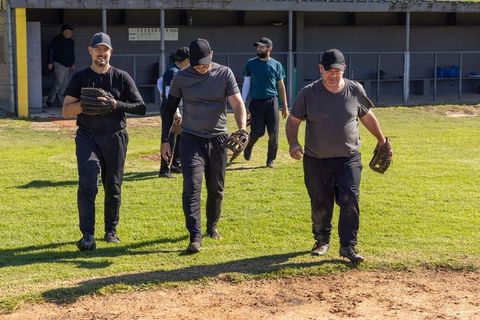 Veteran baseball players walking from dugout holding gloves on sunny field before game
