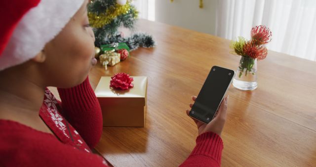 Woman Wearing Santa Hat Using Smartphone with Christmas Gifts on Wooden Table - Download Free Stock Images Pikwizard.com