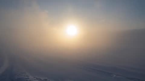 Sun rising through dense fog over snowplain, halo glow and fading tracks, remote winter video