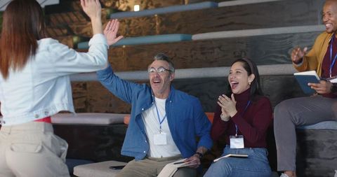 Multicultural team giving high-five during interactive workshop on tiered wooden benches