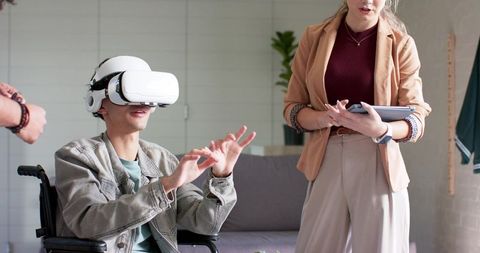 Diverse team assisting man in wheelchair using VR headset while colleague holding tablet