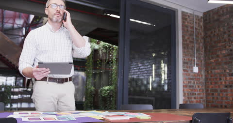 Businessman Making a Call While Consulting Tablet in Office