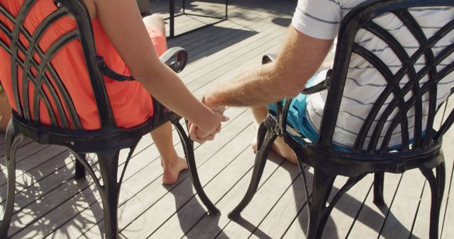 Rear view of a Caucasian couple enjoying time off in summer at a hotel, on the balcony sitting on chairs, holding hands, smiling and interacting.
