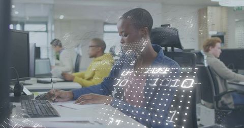 Focused woman writing notes at open office desk with digital code overlay, teamwork