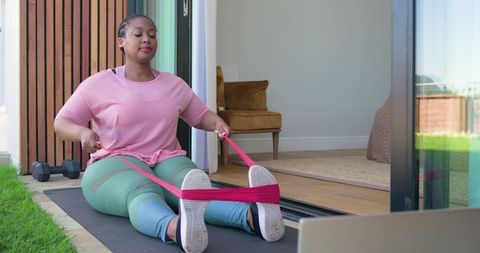 Mid adult african american woman exercising with resistance loop band at home doorway