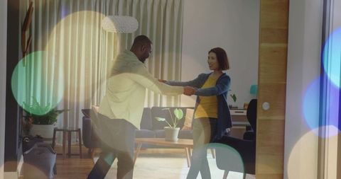 Couple dancing and holding hands in cozy modern living room with warm bokeh lights