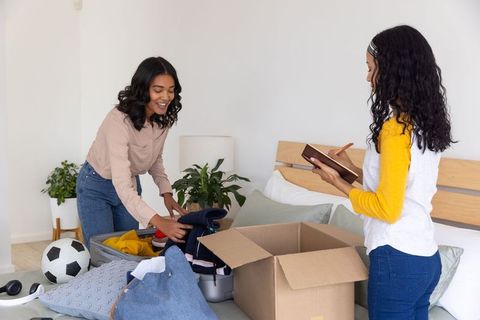 Mother and teen daughter packing suitcase in cozy bedroom, organizing clothes and preparing move