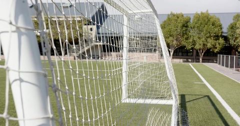 Close-up framing of soccer goal net on artificial turf pitch under bright sunny sky
