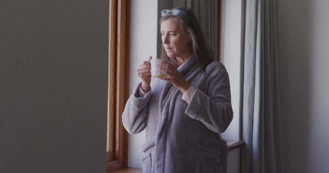 Senior woman in robe enjoying coffee by window at home - Download Free Stock Images Pikwizard.com