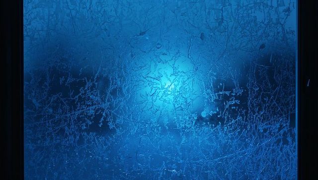 Backlit frosted window with intricate ice crystals glowing blue-cyan ambient light