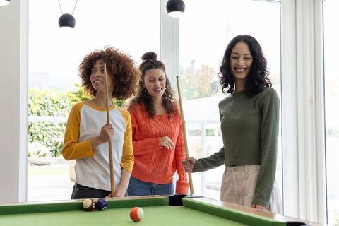 Diverse women playing pool in bright home lounge enjoying casual billiards and social fun