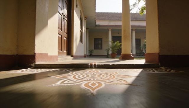 Sunlit kolam on polished veranda floor with heritage courtyard entrance and columns