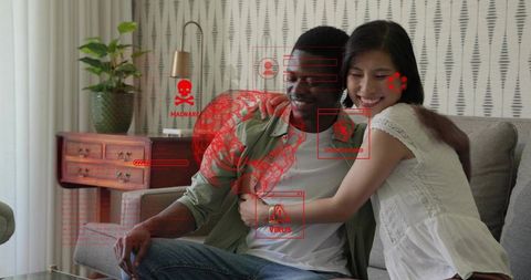 Interracial couple hugging on sofa, smiling with malware overlay illustrating cyber threats