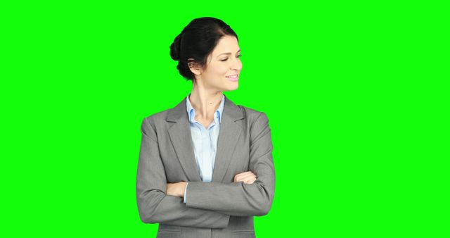 Confident businesswoman smiling and looking away with arms crossed, wearing a professional suit on green screen background. Ideal for corporate presentations, advertisements, or promotional materials related to business, leadership, and professionalism.