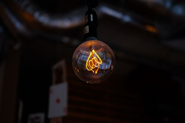 This close-up of a glowing Edison bulb in a dark, industrial setting can be used to emphasize themes of vintage design, interior decoration, and warm lighting. This image is ideal for use in articles or advertisements focused on retro lighting, industrial interiors, or stylish home decor.
