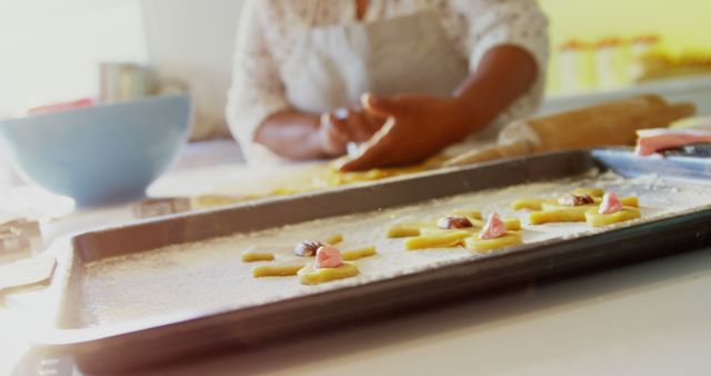 Photo depicting female hands preparing homemade cookies in a kitchen. Dough is being shaped on a surface while a baking tray with unbaked cookies is ready. Ideal for content related to home baking, cooking tutorials, recipe blogs, culinary arts, and kitchen activities. Could be used in advertisements for baking products or any content promoting homemade and artisanal foods.