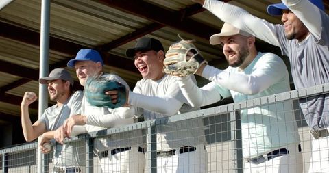 Baseball team cheering in dugout celebrating win with gloves raised and high energy