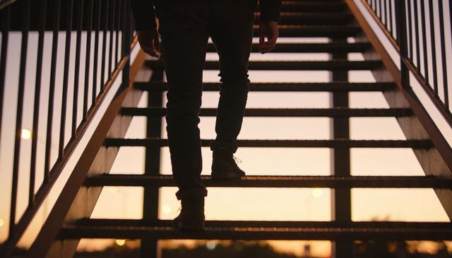 Ascending metal staircase at sunset dusk silhouette of person climbing urban stairs