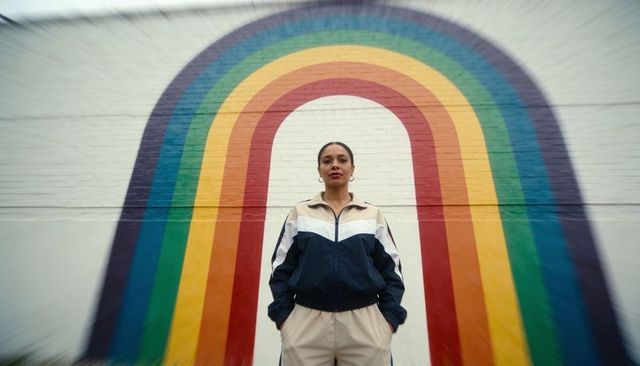 Confident woman standing in front of rainbow mural wearing colorblock windbreaker