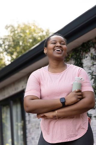 African american woman smiling and holding water bottle after workout outdoors