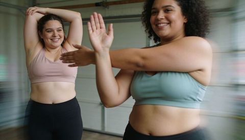 Plus size women stretching and smiling during home gym workout in garage studio