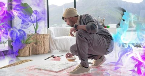 Indian painter crouching mixing paint on canvas in airy studio with mountain view