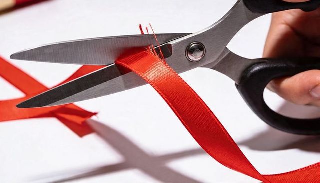 Scissors cutting red satin ribbon close-up studio lighting hand gripping handle