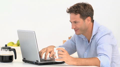 Man Drinking Coffee While Working on Laptop at Home