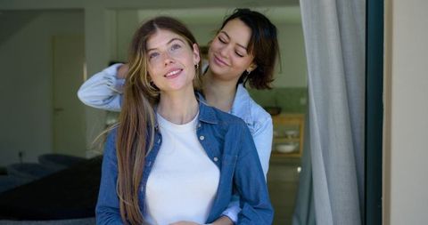 Female couple embracing at home doorway in soft daylight, denim shirts, intimate lifestyle
