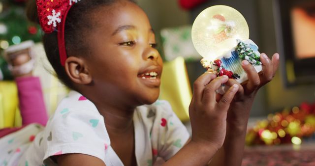 This image of a joyful child holding a snow globe can be used for festive holiday promotions, Christmas cards, holiday season advertisements, and family-oriented content. It captures the excitement and magical feeling of Christmas, perfect for adding warmth and cheer to any holiday-related project.