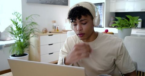 African american man working remotely at kitchen table wearing beanie and headphones