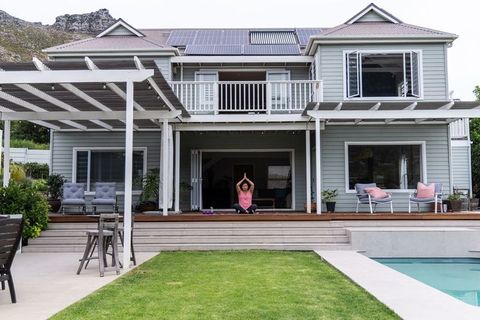 Woman meditating on wooden deck by pool with pergola and solar-powered modern home