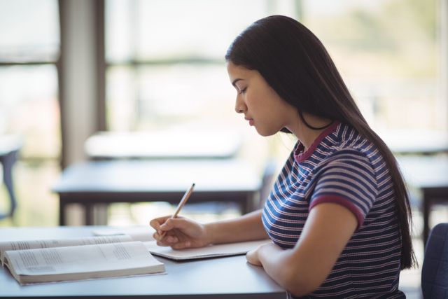 Young schoolgirl concentrating on her studies in a classroom. Ideal for educational content, school promotions, academic articles, and learning resources.