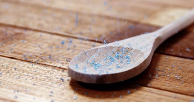 A wooden spoon is sprinkled with blue particles on a textured wooden surface, with copy space. It suggests a cooking or baking activity, involving decorative elements like colored sugar or edible glitter.