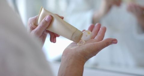 Mature woman squeezing lotion from tube for skincare routine