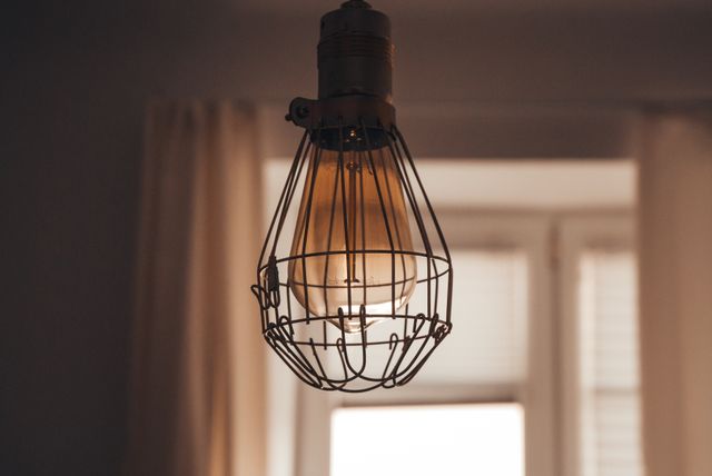 Vintage industrial hanging light bulb pendant glowing in a dimly lit room. Ideal for use in articles on interior design, home decor trends, lighting ideas, and vintage style inspiration. Great for blogs, social media, and advertisements showcasing lighting solutions or home renovation projects.
