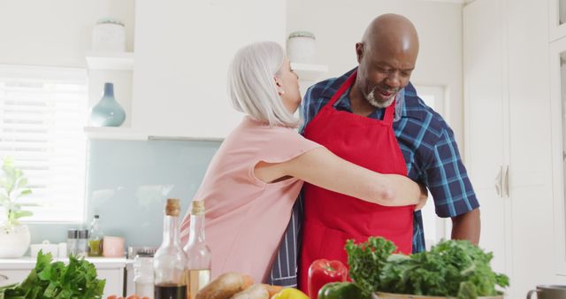 Senior couple hugging in modern kitchen while preparing fresh vegetables. Perfect for depicting healthy lifestyle, elderly romance, home cooking, and wholesome family moments.