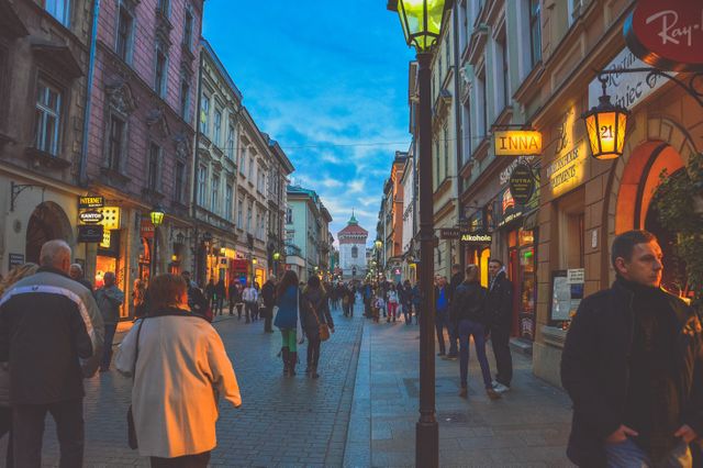 Street scene in a European city at dusk with lively atmosphere. Pedestrians fill the street, enjoying the beautiful historic architecture and illuminated storefronts. Perfect for themes related to travel, city living, urban exploration, and European tourism.