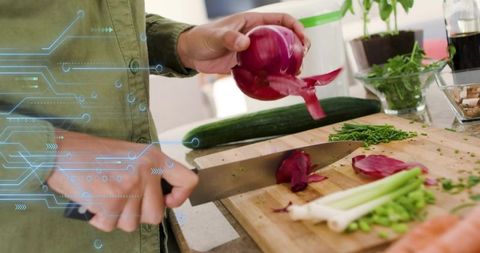 Woman chopping red onion with chef knife on wooden board wearing green shirt tech overlay