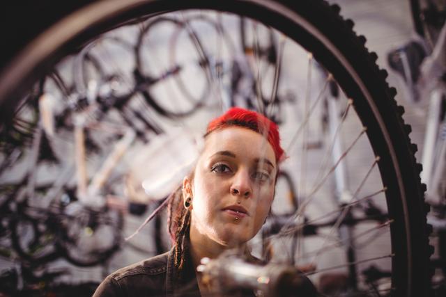 Woman mechanic with red hair is closely examining a bicycle wheel in a workshop. Ideal for use in content related to bicycle repair services, professional mechanics, manual labor, and industrial settings. Can be used for promotional material for bike shops, repair services, or educational content on bike maintenance.