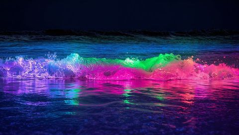 Breaking neon wave crest glowing on dark shore with vibrant multicolor reflections