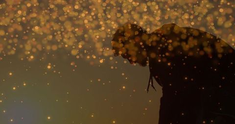 Leaning man bending forward on stage wearing hoodie amid golden bokeh moody silhouette