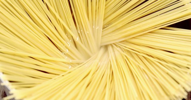 A close-up view of uncooked spaghetti noodles fanned out in a radial pattern, highlighting the texture and uniformity of the pasta. This arrangement emphasizes the simplicity and potential of a basic ingredient in culinary arts.