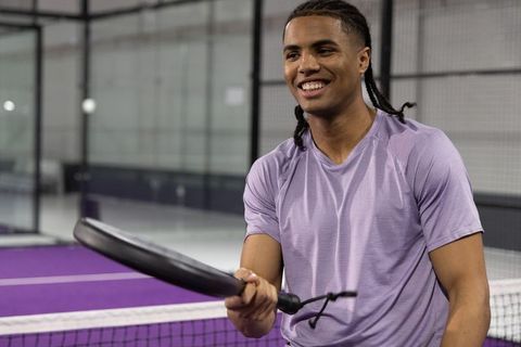 Smiling african american padel player holding racket on vibrant purple indoor court