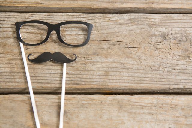 Overhead view of eyeglasses and mustache on wooden table