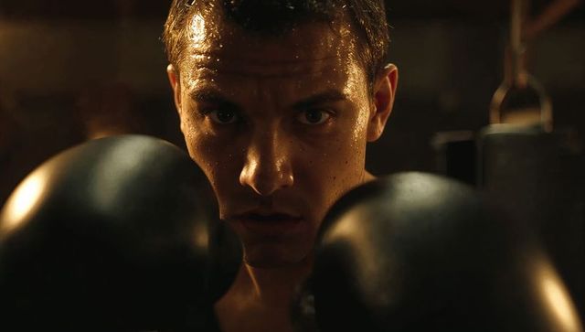 Boxer focusing intently holding black gloves in dim gym