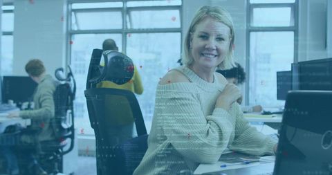 Smiling woman typing and collaborating in open-plan tech office with code overlay