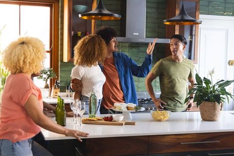 Multiracial friends gathering around kitchen island enjoying wine, snacks and laughter