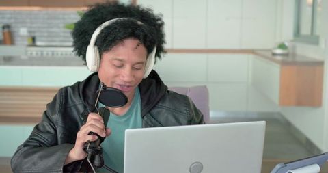 Young creator podcasting in modern kitchen with laptop and studio microphone
